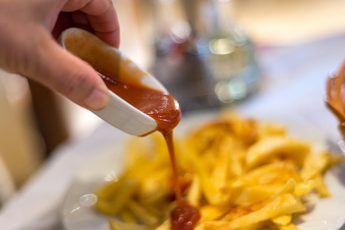 Tomato ketchup being poured over French fries